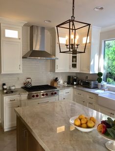 a large kitchen with white cabinets and marble counter tops, an island in the middle has two bowls of fruit on it