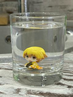 a small doll sitting on top of a glass filled with water and floating in it