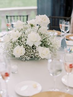 white flowers and baby's breath in a vase on a table with wine glasses