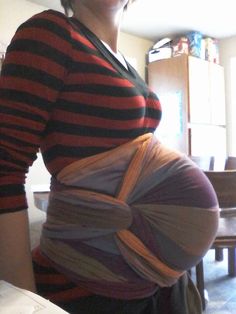 a pregnant woman with her belly wrapped in strips and wearing a striped shirt, standing in front of a dining room table