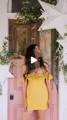 a woman standing in front of a pink door wearing a yellow dress and white stars