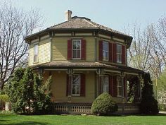 an old victorian house with red shutters on the front and second story, surrounded by lush green grass