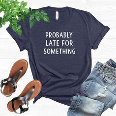 a t - shirt that says probably late for something next to some shoes and a plant