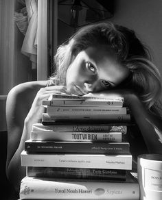 a woman leaning her head on top of a stack of books in black and white