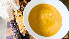 a white bowl filled with soup next to corn on the cob and pumpkins