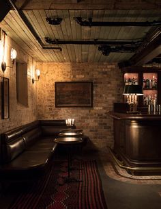 a dimly lit bar with two tables and stools in the corner, next to a brick wall