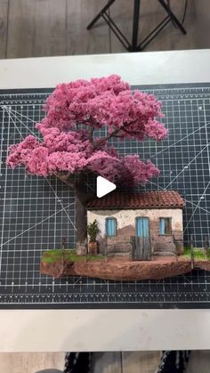 a tree is growing out of the ground next to a house with pink flowers on it