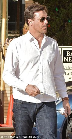 a man in white shirt and jeans walking down the street