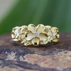 a gold ring with flowers on it sitting on top of a piece of rock next to a plant