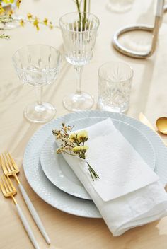 a table set with white plates, silverware and yellow flowers in vases on it