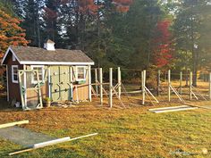 an outhouse in the middle of a field surrounded by trees and fence posts with fall foliage around it