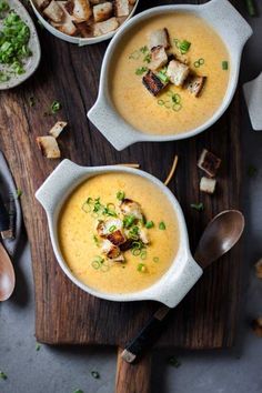 two bowls filled with soup on top of a wooden cutting board next to other dishes