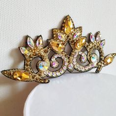 a gold tiara with crystal stones on the top and sides is sitting on a white surface