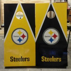 two nfl cornhole game boards with pittsburgh and steeles logos painted on them, sitting in front of a building