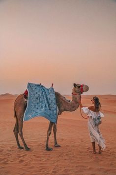 a woman is walking with a camel in the desert