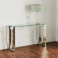 a glass and metal console table with a lamp on it's side in an empty room