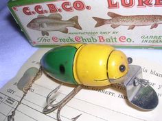 a yellow and green fishing lure sitting on top of a piece of paper next to a box