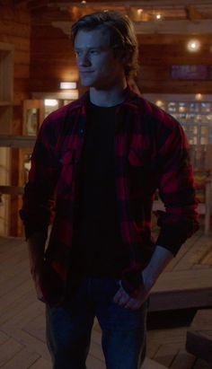 a young man standing in front of a wooden floor with his hands in his pockets