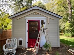 a small white shed with a red door and ladder next to the front door,