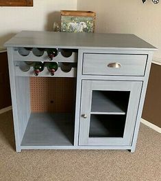 a gray cabinet with wine bottles on top and shelves below it in a room that has carpeted flooring