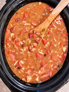 a wooden spoon in a slow cooker filled with beans and meats, ready to be cooked