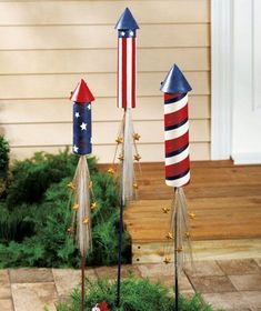 three patriotic decorations in the shape of rockets on top of grass next to a house