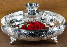 a silver plate with red roses in it on a wooden table next to a bottle