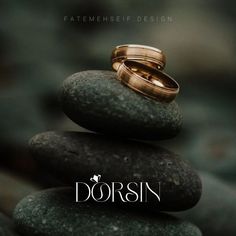 two gold wedding rings sitting on top of rocks with the words dorsin in front of them