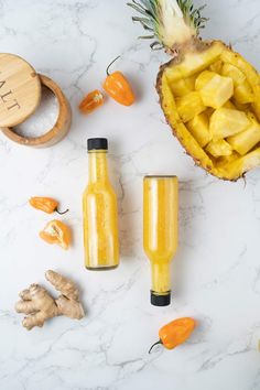 pineapple juice in glass bottles next to sliced oranges and ginger on marble countertop