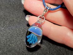 a hand holding a glass pendant with blue flowers in it