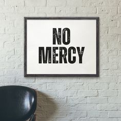 a black chair sitting in front of a white brick wall with a sign that says no mercy on it