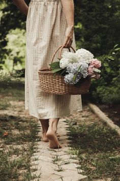 a woman walking down a path holding a basket with flowers in it and wearing sandals