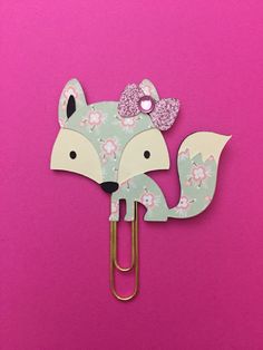 a paper clip with a fox design on it and a bow in the middle, against a pink background