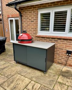 an outdoor bbq with a red grill on it's top and two windows