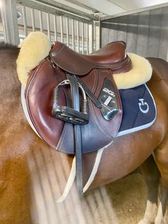 a brown horse with a saddle on it's back in a stable, looking down at the ground