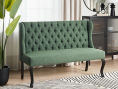 a green couch sitting on top of a wooden floor next to a potted plant