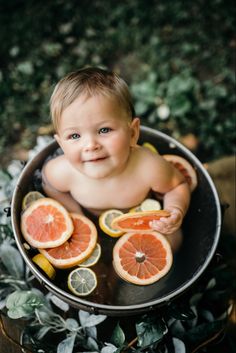 a baby sitting in a pot filled with oranges