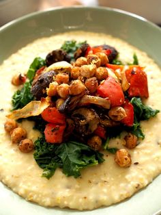 a white plate topped with hummus, tomatoes and other vegetables on top of grits