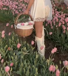 a woman in white dress carrying a basket full of pink tulips on field