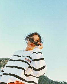 a woman wearing sunglasses and a striped shirt is holding her camera up to her face