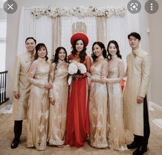 a group of people standing next to each other in front of a white wall with flowers