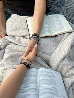 two people holding hands over an open book on top of a bed covered in blankets