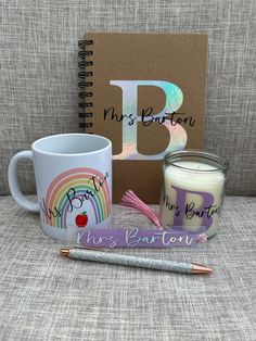 a mug, notebook and pen sitting on a couch next to a notepad with the letter b