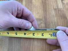 a person holding a pair of scissors on top of a wooden table next to a measuring tape