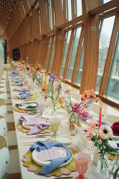 a long table is set with colorful plates and place settings for an elegant dinner party