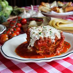 a white plate topped with lasagna covered in sauce and cheese on top of a checkered table cloth