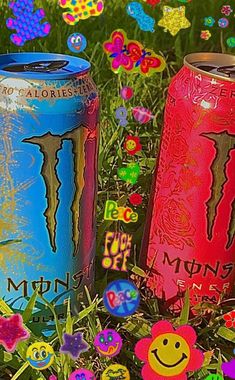 three colorful cans sitting on top of a lush green field covered in lots of flowers