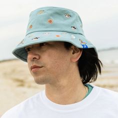 This beautifully embroidered bucket hat details all kinds of beach life found in sand, sea and sky. Can you spot the Piping Plover? You'll also see Horseshoe Crabs, Ruddy Turnstones, Red Knot, Striped Bass and flounder. Playful Blue Bucket Hat For Vacation, Summer Beach Bucket Sun Hat, Spring Bucket Hat For Beach, Fun Curved Brim Bucket Hat For Beach, Playful Bucket Hat For Beach, Blue Fun Bucket Hat For Summer, Fun Blue Bucket Hat For Vacation, Playful Bucket Cap For The Beach, Playful Beach Bucket Hat