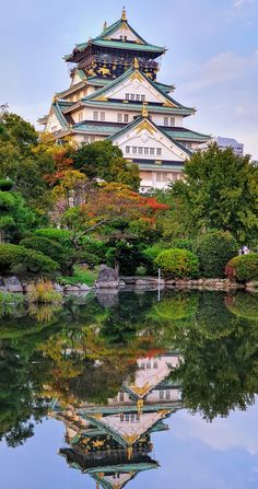 a large building sitting on top of a lush green hillside next to a lake in front of trees