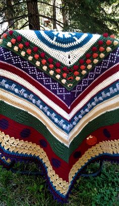 a crocheted blanket sitting on top of a green grass covered ground next to trees